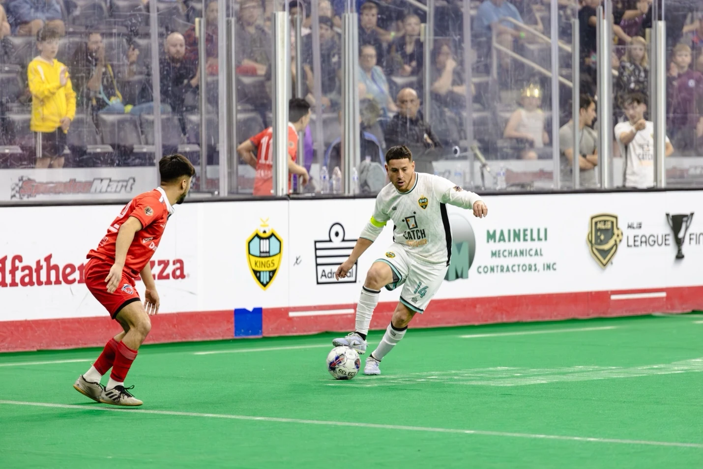 Indoor soccer players competing on green arena turf in front of a full crowd